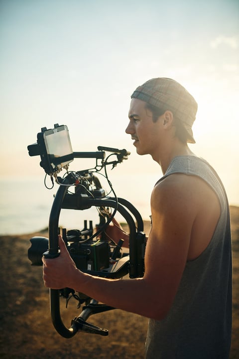 Shot of a focused young man shooting a scene with a state of the art video camera outside on a beach during the day