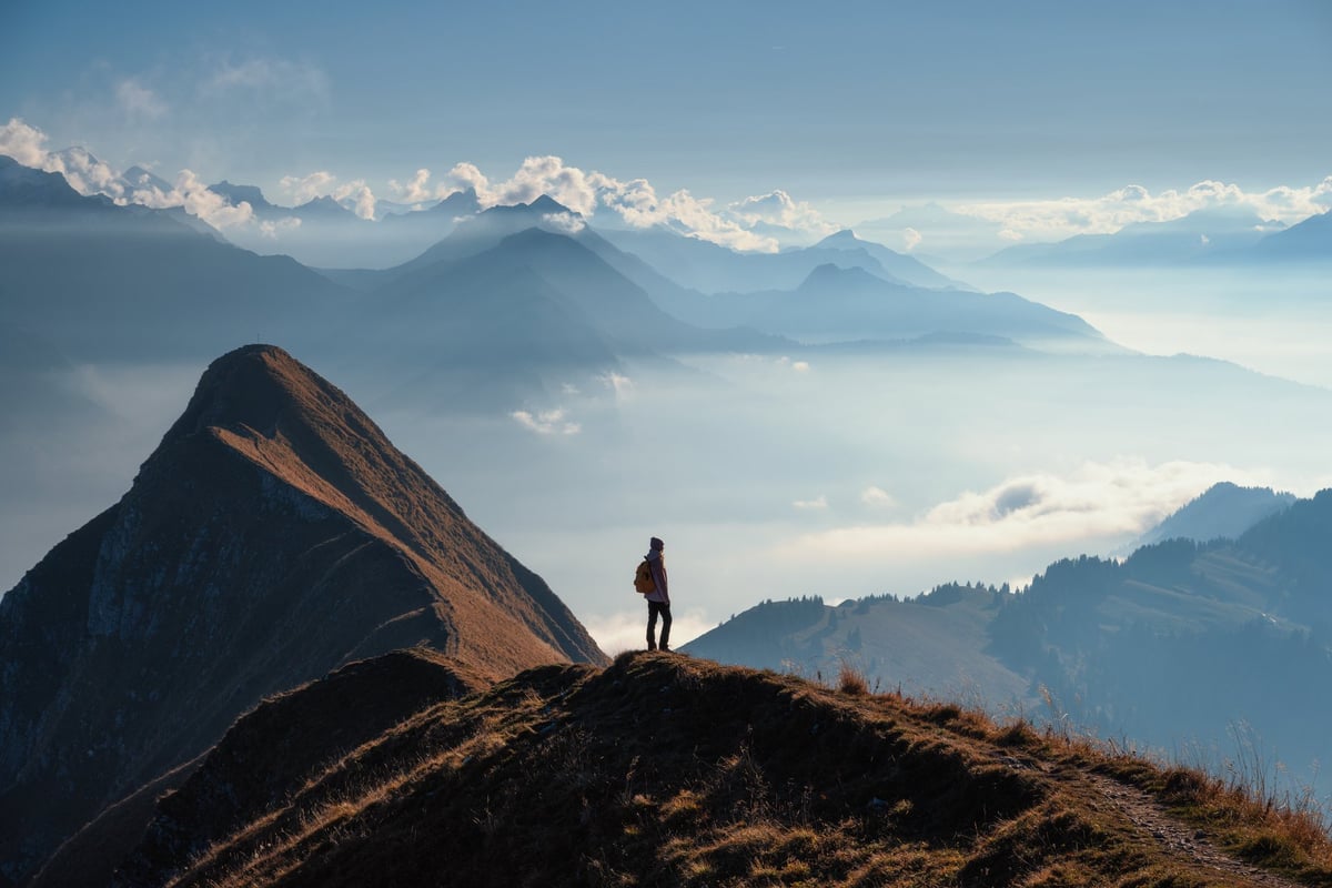 Hiker with backpack standing on a high mountain ridge above clouds at sunrise