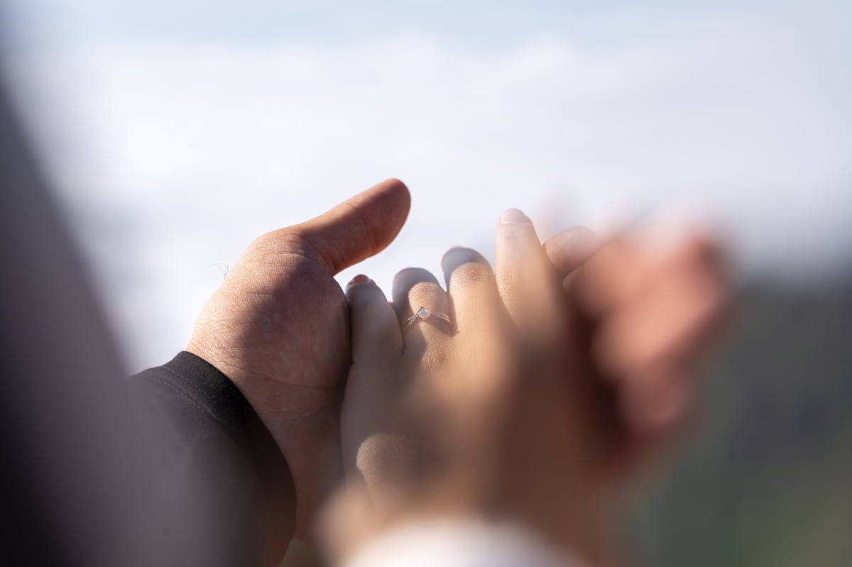 Engaged couple holding hands with a ring in an outdoor setting
