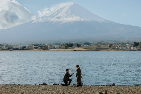 Man proposing to woman on beach with snow-capped Mount Fuji in background across the lake