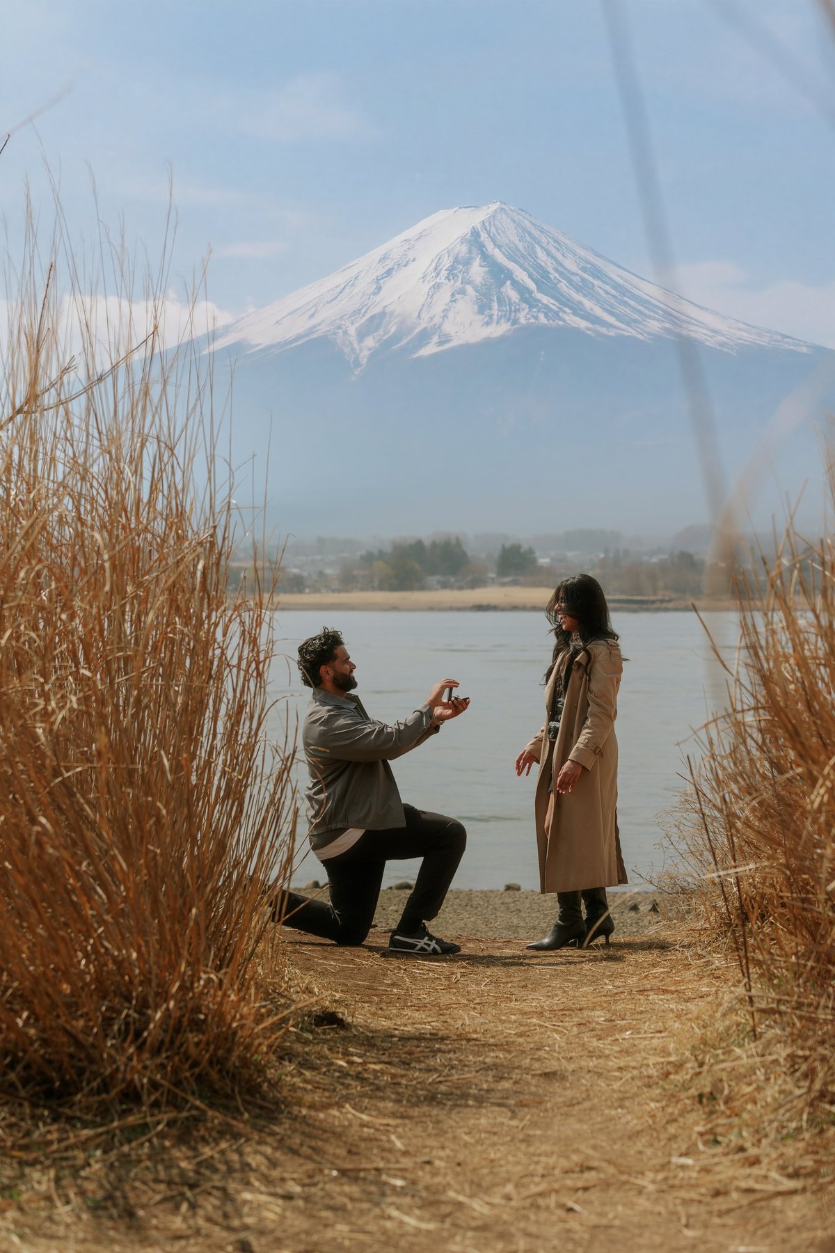Man proposing to woman on beach with snow-capped Mount Fuji and lake in background