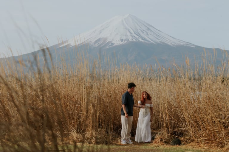 Couple standing in dried grass field with snow-capped Mount Fuji in background