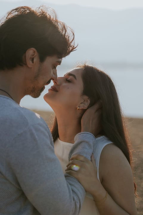 Couple about to kiss on a beach at sunset, facing each other intimately with ocean in background