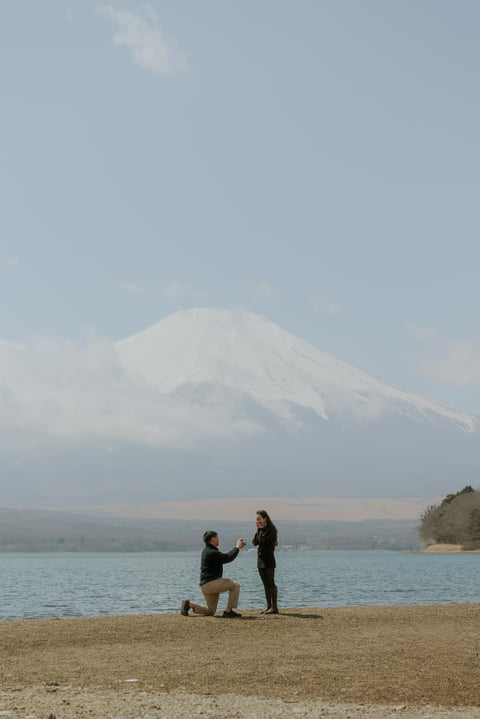 Man proposing to woman on beach with snow-capped Mount Fuji in background