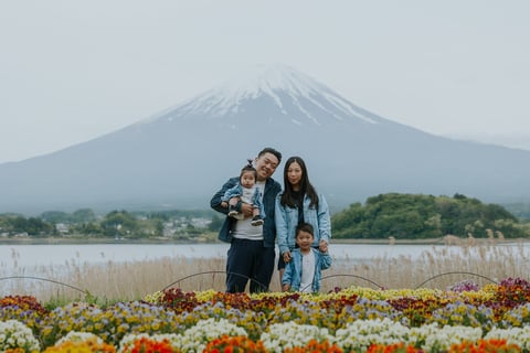Family of four posing in a flower field with a snow-capped mountain and lake in the background