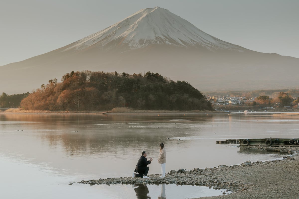Two people wading in a misty lake with snow-capped Mount Fuji and forested island in the background