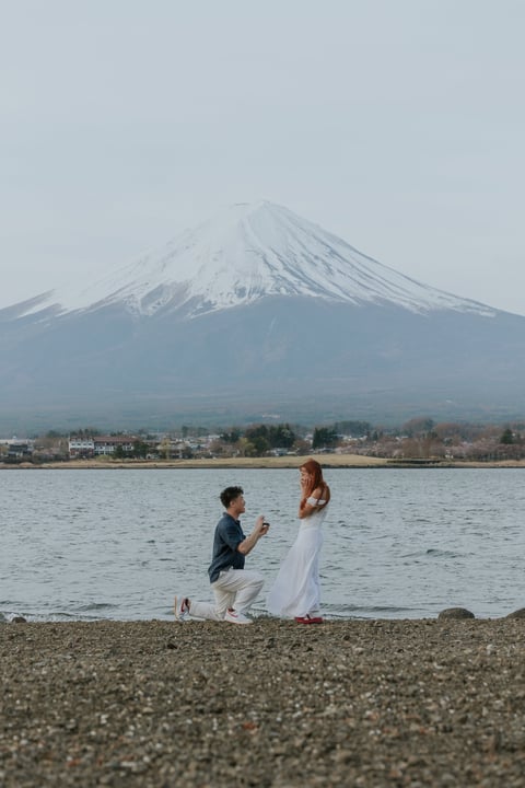 Man proposing to woman on beach with snow-capped Mount Fuji in background