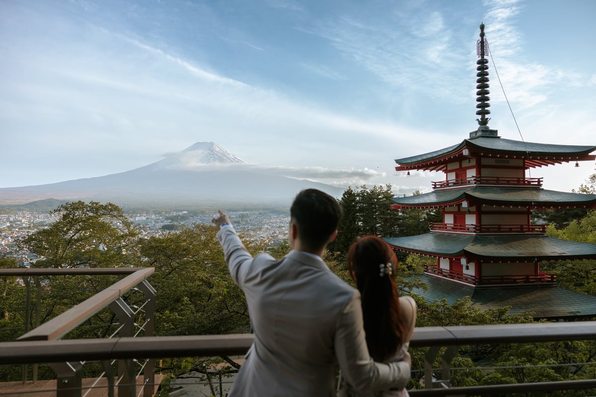 Couple viewing Mount Fuji from observation point with red pagoda and forested landscape in foreground