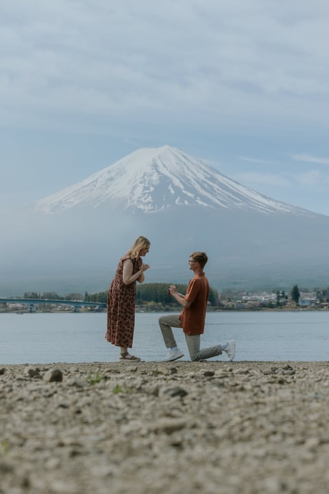 Man on knee proposing to woman on beach with Mount Fuji and lake in background