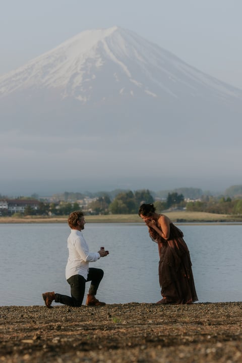 Man kneeling on beach proposing to woman with snow-capped mountain in background